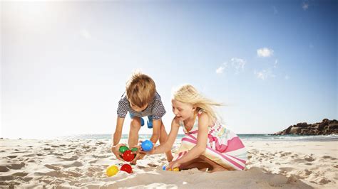 Niños jugando en la playa con camisetas de protección solar y escarpines, mostrando la seguridad y comodidad.