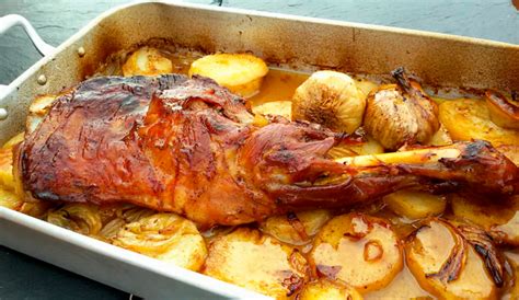 Plato servido de paletilla de cabrito asada al horno con guarnición de patatas y hierbas aromáticas