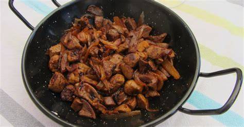 Fotografía de un plato tradicional de asadura de cabrito encebollada servido en una cazuela de barro