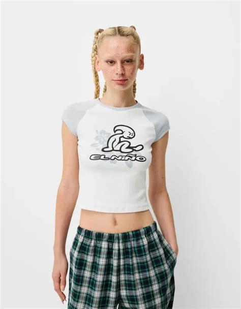 Variedad de prendas de la colección Bershka x El Niño, mostrando camisetas, tops, faldas y gorras con el logo y estética de la marca.