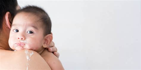 Bebé regurgitando leche, con un padre consolándolo