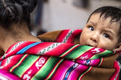 Foto de una mujer indígena con un bebé en un portabebés tradicional, mirando hacia adelante