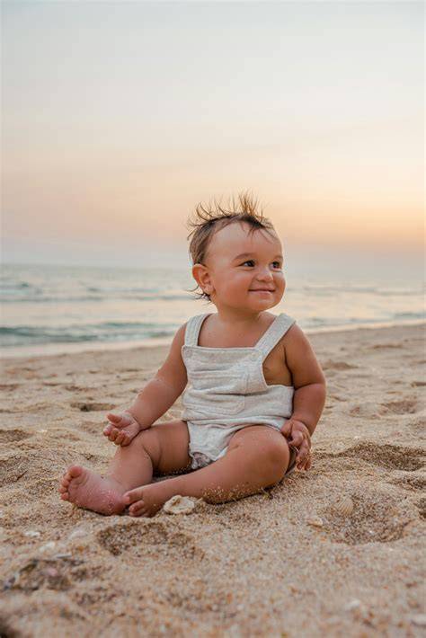 Bebé con un traje de neopreno sentado en la arena de una playa.