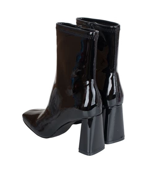 Imagen de primer plano de unos botines de charol negro con el característico tacón chupete, destacando el brillo del material.