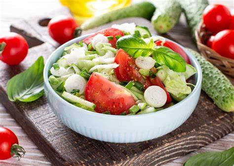 Fotografía cenital de la ensalada terminada servida en un bol, mostrando el contraste de colores entre el melón naranja/verde, el queso blanco y el verde de las hierbas.