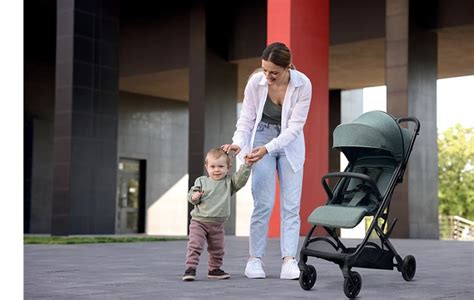 Madre manejando una silla de paseo ligera con una mano mientras sostiene una bolsa de la compra en la otra