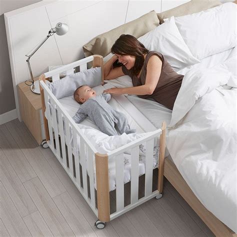 Imagen de una cuna de colecho colocada junto a la cama de matrimonio, con un bebé durmiendo plácidamente en ella.